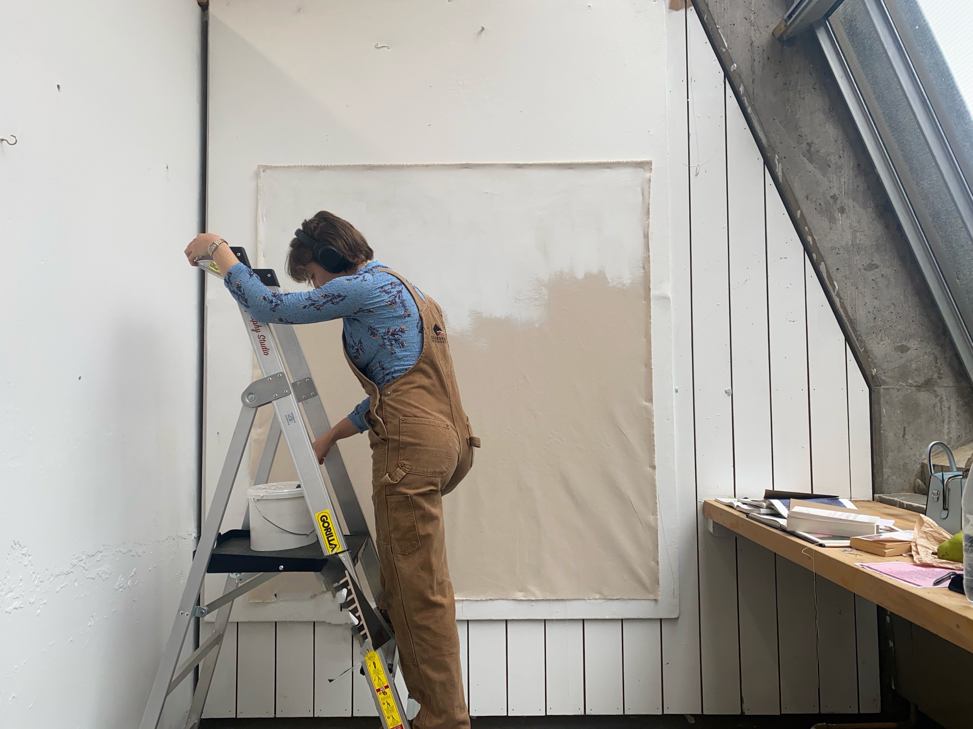 Stephanie Postles on a stepladder in her studio, working on a large unstretched canvas.